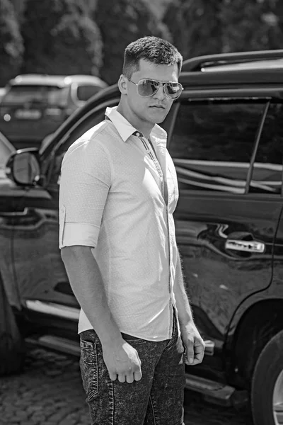 Mann steht neben Auto auf Stadtstraße. Geschäftsmann mit stylischer Sonnenbrille im sonnigen Freien. Fahrer im Autotransport. Reise- und Transportkonzept — Stockfoto