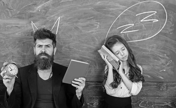 Time to learn concept. Teacher devil and sleepy girl. Bearded man with alarm clock and book. Little child student tired of study in school. Tutor and schoolgirl with chalkboard drawings