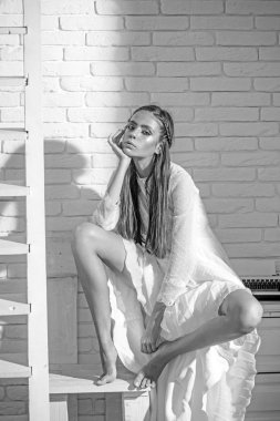 Beyaz bahar yaz elbiseli genç kadın. Bir tuğla duvar arka plan üzerinde poz kız. Yaz kıyafeti. Şık saç modeli. Moda fotoğraf. Renkli makyaj ile oturan seksi Bayan