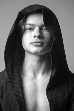 Siyah hood, gri arka planda emin yüz adam. Pürüzsüz cilt yüz, boyun ve göğüs kameraya bakarak üzerinde olan adam. Maço siyah bornoz ile kukuleta, yakın çekim. Erkeklik kavramı.