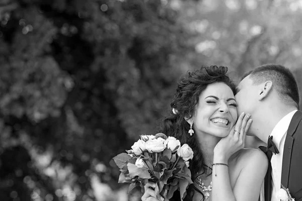 Kersverse man kus gelukkige vrouw met boeket. Jonggehuwde paar glimlach op zomer buiten — Stockfoto