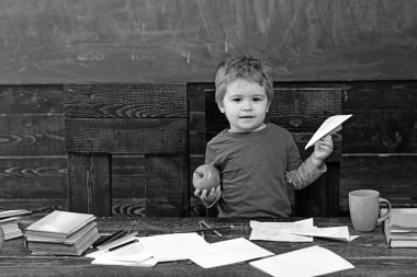 Kağıt Uçak ve elma sınıfta küçük çocuk. İlköğretim okulunda evlat. Copybooks, kitap ve Kupası ile masanın arkasında şirin çocuk