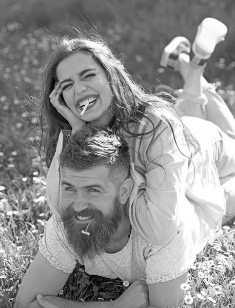 Man and woman laying on grass spring day. Couple on smiling faces smoking outdoors, nature on background. Smoking habit concept. Couple in love spend time outdoors and smoking. — Stock Photo, Image