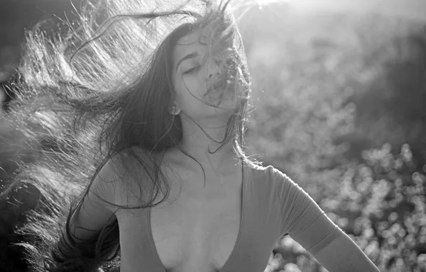 Woman on calm face enjoy sunny and windy day, nature on background, defocused. Girl with decollete enjoy her hair waving by wind. Lady looks attractive with waving long hair. Hair care concept.