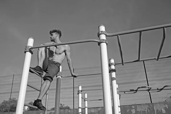 Sportman met kale romp monkey bars bovenop. Man atleet klimmen op metalen jungle gym op blauwe hemel. Macho ontspannen na training buiten. Sport, gezondheid en energie concept — Stockfoto