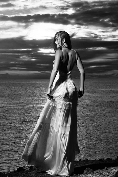 Красивая девушка в белом платье стоит на берегу темного моря — стоковое фото