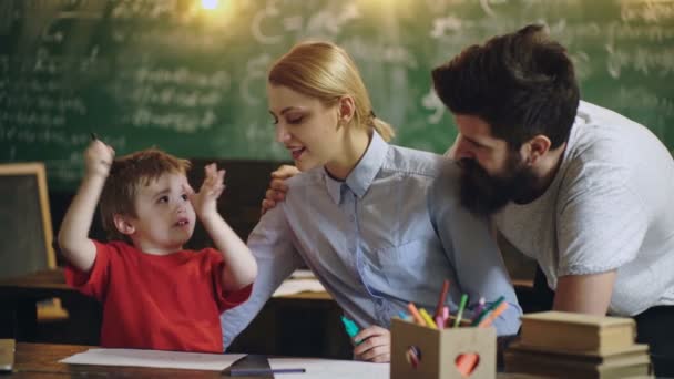 Eltern und ihr Sohn malen in einem Klassenzimmer vor dem Hintergrund einer grünen Tafel. zurück zur Schule. Kind im Unterricht. Lustiges Kind gegen Tafel. Nerd-Kind hat Spaß. — Stockvideo