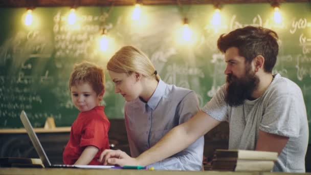 Föräldrar med sin son arbetar med laptop sitter i klassrummet på bakgrund av en grön styrelse. Familj i klassrummet. Tillbaka till skolan. Lärande koncept. Lärare och elev. — Stockvideo