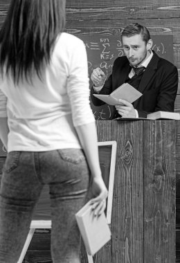 Esmer kız kitap onun elinde tutarak geri dön. Sıkı öğretmen Kürsüsü, ayakta iken kadın onun öğrencisi bakarak.