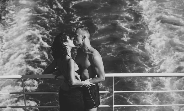 Attraktives Paar küsst und genießt den Sommerurlaub. Flitterwochen, frisch verheiratet. Paar steht an Deck eines Kreuzfahrtschiffes mit Meereswellen im Hintergrund. Verliebtes Paar auf Kreuzfahrtschiff unterwegs. — Stockfoto