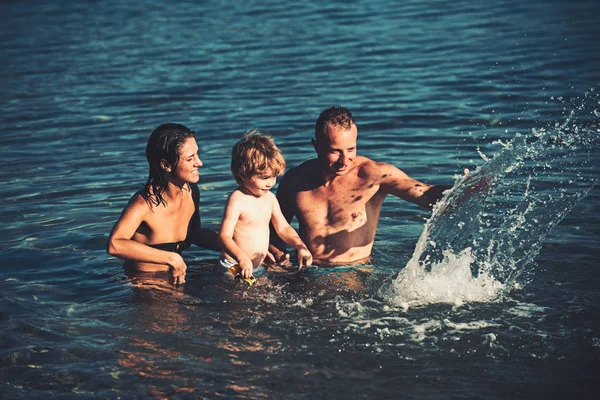 Familia feliz en un mar que se divierte y salpica el agua en verano . — Foto de Stock