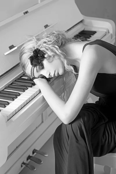 Beautiful blond girl in headband lying on keyboard of white piano with her eyes closed. Back to 1920s — Stock Photo, Image