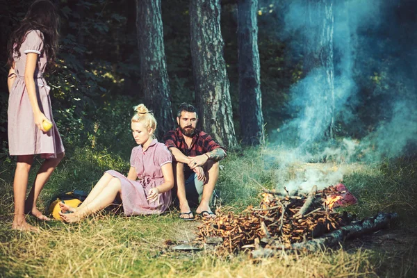 妇女和男子在营地火灾的老式风格。朋友们在篝火旁放松。人们在篝火圣火在绿色森林。露营, 远足和旅行。暑假概念 — 图库照片