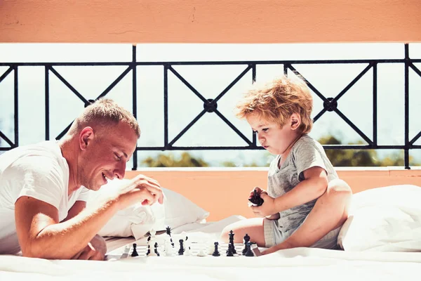 Padre con hijo en el balcón jugar al ajedrez. Un niño juega ajedrez con su padre. Vacaciones de verano de familia feliz. Viajar en familia con niños el día del padre. El amor y la confianza como valores familiares —  Fotos de Stock