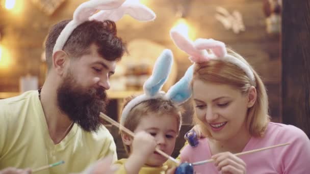 Gros plan d'une famille qui peint des œufs de Pâques. Mère, père et fils peignent des œufs. Une famille heureuse se prépare pour Pâques. Mignon petit garçon enfant portant des oreilles de lapin. Joyeuse Pâques . — Video