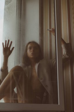 Pencerenin yanında sütyensiz, üzgün, seksi bir kadın..