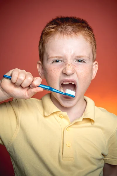 Bonito rapaz engraçado com uma escova de dentes. Um rapazinho feliz a lavar os dentes. Menino adorável segurando escova de dentes e sorrindo para a câmera isolada no vermelho. Higiene dentária . — Fotografia de Stock