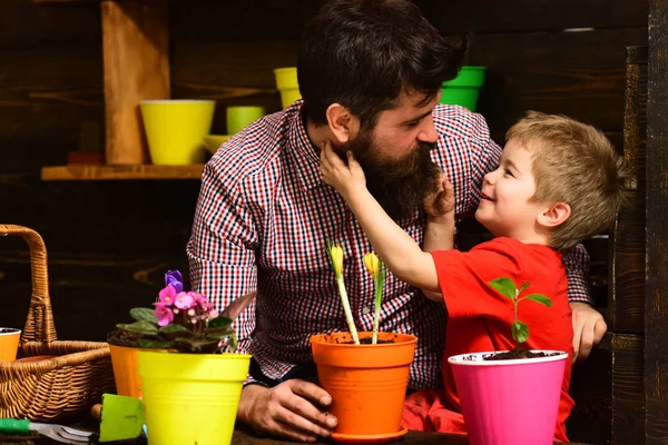 Happy gardeners with spring flowers. bearded man and little boy child love nature. Father and son. Fathers day. Flower care watering. Soil fertilizers. Family day. Greenhouse. Work for you — Stock Photo, Image