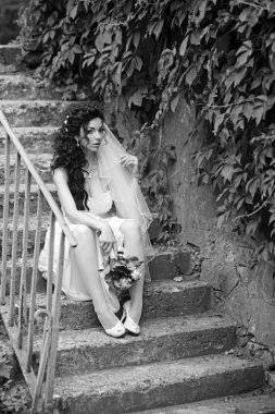 Güzel düğün kutlama. Zarif dantel gelinlik bir kolye ve Gelin Buketi Gelin taş merdiven üstünde oturuyor. Düğün Giyim, aksesuar