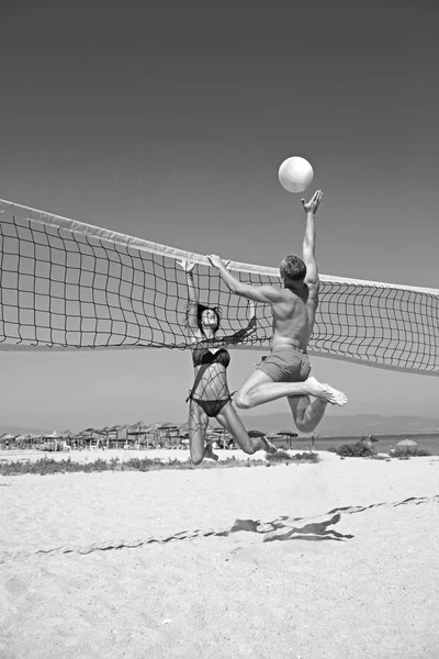 People playing beach volleyball having fun in sporty active lifestyle. Man hitting volley ball in game in summer. Woman and man fitness model living healthy lifestyle doing sport on beach