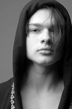 Maço siyah bornoz ile kukuleta, yakın çekim. Siyah hood, gri arka planda emin yüz adam. Erkeklik kavramı. Pürüzsüz cilt yüz ve boyun kameraya bakarak üzerinde olan adam.