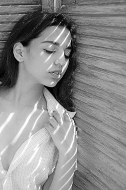 Sakin yüz turkuaz kanepe üzerinde yalın kız. Kadın esmer standları jaluzi, güneş ışığı ve gölge yüzünde çizgili yakınındaki ise tüyler ürpertici. Isı kavramı. Bayan açılarak gömlek giyer.