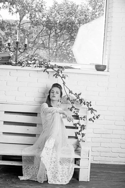 Una joven con un vestido blanco está sentada en un banco. mujer en un vestido elegante. Verano moda look . — Foto de Stock