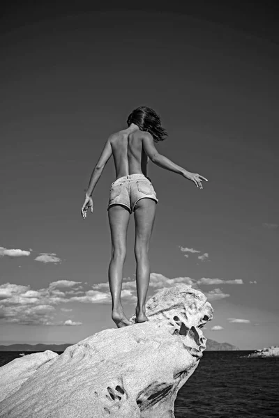 性感的女人在牛仔裤短裤在蓝天背景。女孩在石头上裸泳。暑假和到海洋旅行。马尔代夫或迈阿密海滩。性感的妇女在加勒比海在巴哈马 — 图库照片