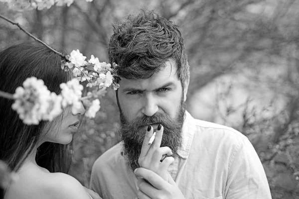 Couple smoking near blooming trees. Female hands holds cigarette for man in garden on spring day. Couple in love spend time in spring garden, branches with flowers on background. Smoking concept. — Stock Photo, Image