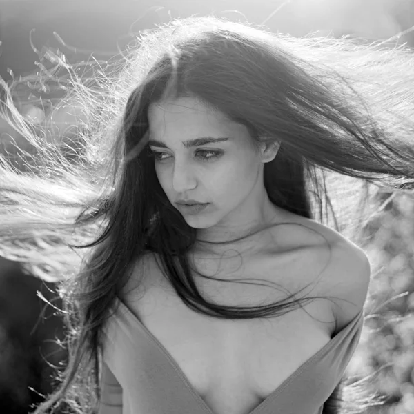 Girl with decollete enjoy her hair waving by wind. Woman on calm face enjoy sunny and windy day, nature on background, defocused. Lady looks attractive with waving long hair. Hair care concept.