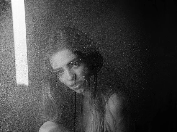 Sexy woman behind plastic sheet with water drops. Window with water drops before girl with makeup. Fashion beauty and love. Rain drops on window glass in heart shape. Shower and hygiene spa treatment