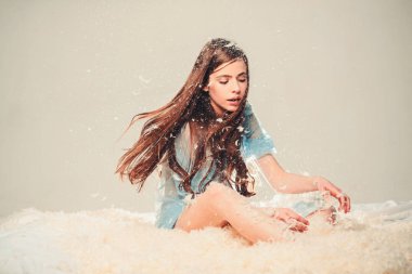 Tüyler, gri arka plan uçmak iken şeffaf mavi Geceliği Bayan yatakta oturur. Kız yatak ve oyun tüy ile meşgul yüz oturur. Hassasiyet kavramı. İhale pijama uzun saçlı kadın.