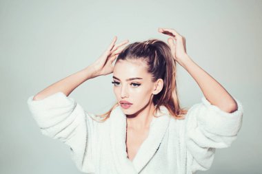 Kadın spa yordamlar için hazırlar ve kuyruğu saç bağları. Spa ve sağlıklı yaşam konsepti. Bayan güzel saç hakkında umurunda değil. Bornoz sakin yüzüne kız onu uzun saçlı, gri arka plan dokunur