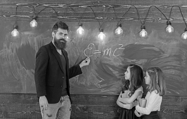 Учитель пишет мелом на доске. Маленькие девочки слушают бородатого мужчину в школьном совете. Преподаватель обучает детей в классе. Учитель и ученики имеют урок в классе. Образование и школа — стоковое фото
