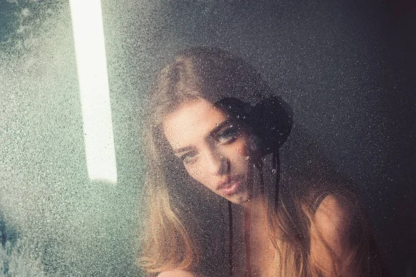 Tratament spa pentru duș și igienă. Femeia sexy în spatele foii de plastic cu picături de apă. Ploaie picături pe fereastră sticlă în formă de inimă. Fereastra cu picături de apă înainte de fata cu machiaj. Frumusețe și dragoste de modă — Fotografie, imagine de stoc