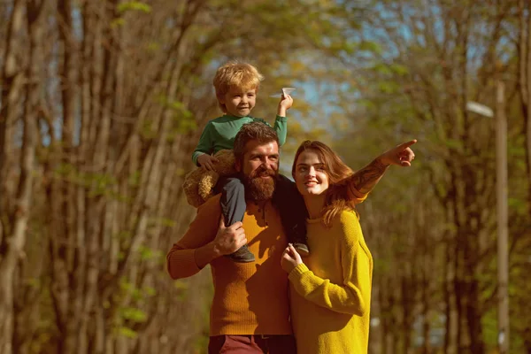 Little son with father and mother launch paper plane in park, travel concept. Happy family plan to travel by plane on vacation. What a flight