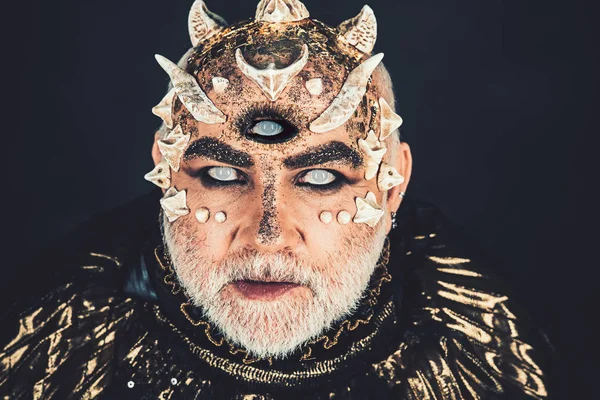 Alien, demon, sorcerer makeup. Horror and fantasy concept. Head with third eye, thorns or warts. Demon on black background, close up. Senior man with white beard dressed like monster in darkness.