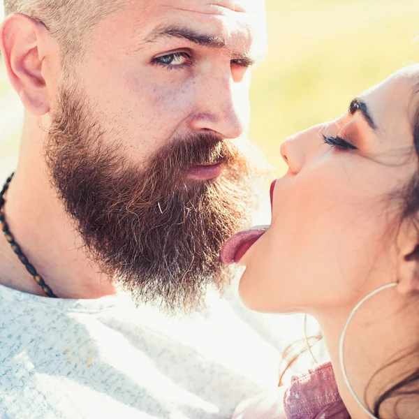 Lady with pink tongue licking bearded macho. Kiss concept. Couple kissing outdoors, nature on background, close up. Couple in love on happy faces relaxing and kissing with tongue