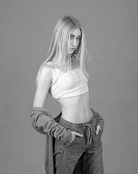 Blond model in yellow top and boyfriend style jeans posing with her hands in pockets isolated on gray background — Stock Photo, Image