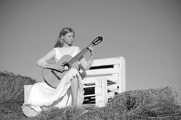 Sensual woman play guitar on wooden bench. Albino girl hold acoustic guitar, string instrument. Fashion musician in white dress on sunny nature. Woman guitarist perform music concert