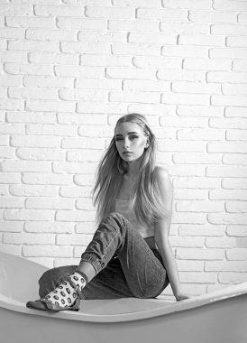 Küvet beyaz tuğla duvar önünde kenarında oturan dağınık saçlı sarışın model