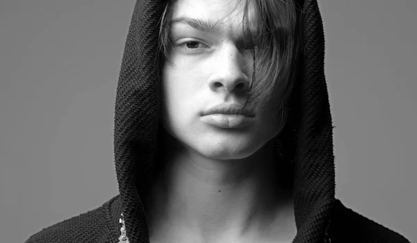 Concepto masculinidad. Macho en albornoz negro con capucha, de cerca. Tipo con cara confiada en capucha negra, fondo gris. Hombre con la piel lisa en la cara y el cuello mirando a la cámara . —  Fotos de Stock