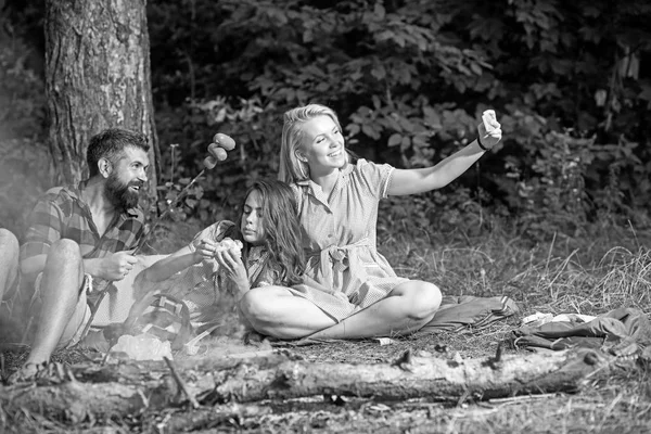 Женщина делает фото или видео со смартфоном в лесу. Друзья делают селфи с сосисками у костра. Бойфренд и подружки улыбаются для мобильного телефона. Новые технологии и современная жизнь, винтаж — стоковое фото