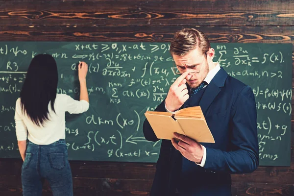 Estudante do sexo feminino resolvendo equação no conselho. Jovem professor com cerdas curtas ajustando óculos enquanto lê um boo — Fotografia de Stock