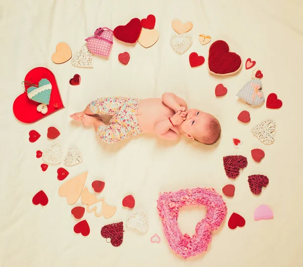 Cute baby girl. Childhood happiness.Valentines day. Love. Portrait of happy little child. Small girl among red hearts. Sweet little baby. New life and birth. Family. Child care