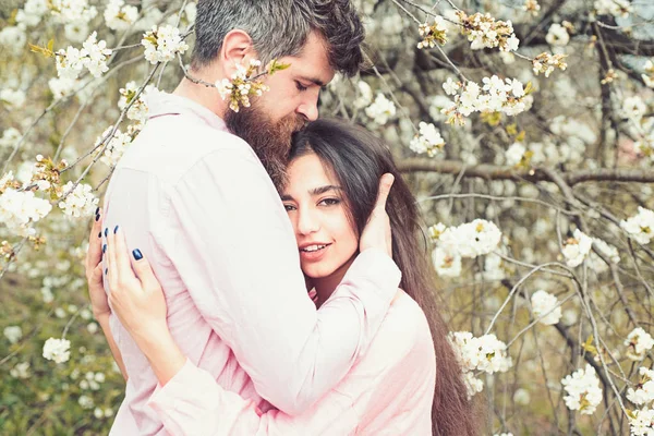 Par i kärlek tillbringa tid i vårträdgård, grenar med blommor på bakgrunden. Vårens datum koncept. Par kramar nära blommande träd. Mannen och kvinnan kramar i blommande trädgård vårdag. — Stockfoto