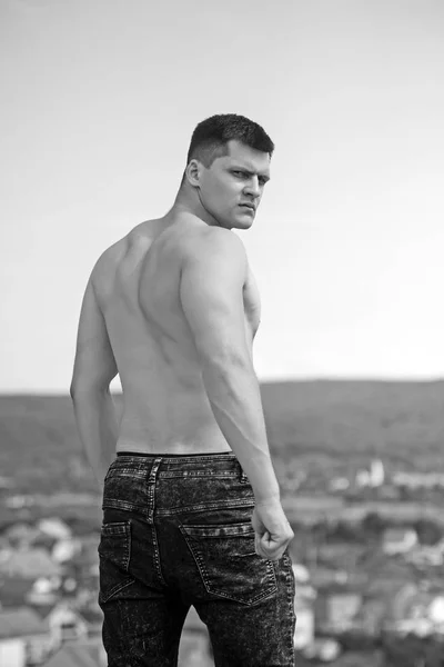 Culturista con torso ajustado de nuevo en jeans. Hombre atleta en montaña en el cielo azul. Actividad de entrenamiento y entrenamiento. Deporte en vacaciones y concepto de actividad — Foto de Stock