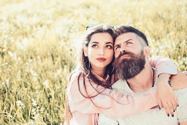 Homem com barba e mulher senta-se no dia de primavera grama. Conceito de lazer primavera. Casal em rostos sonhadores felizes sentados no prado, natureza no fundo. Casal apaixonado passar o tempo ao ar livre e abraços . — Fotografia de Stock