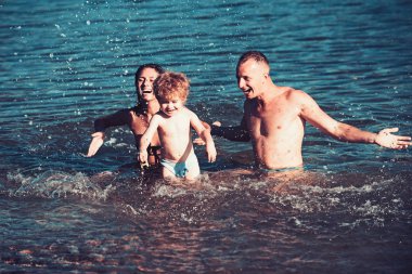 Mutlu genç aile ile küçük çocuk kumsalda eğleniyor. Neşeli bir aile. Seyahat ve tatil. Yaz tatillerini.