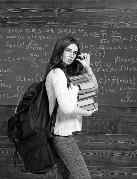 Porträtt av ung brunett student med högen av böcker och tung ryggsäck holding hennes glasögon — Stockfoto